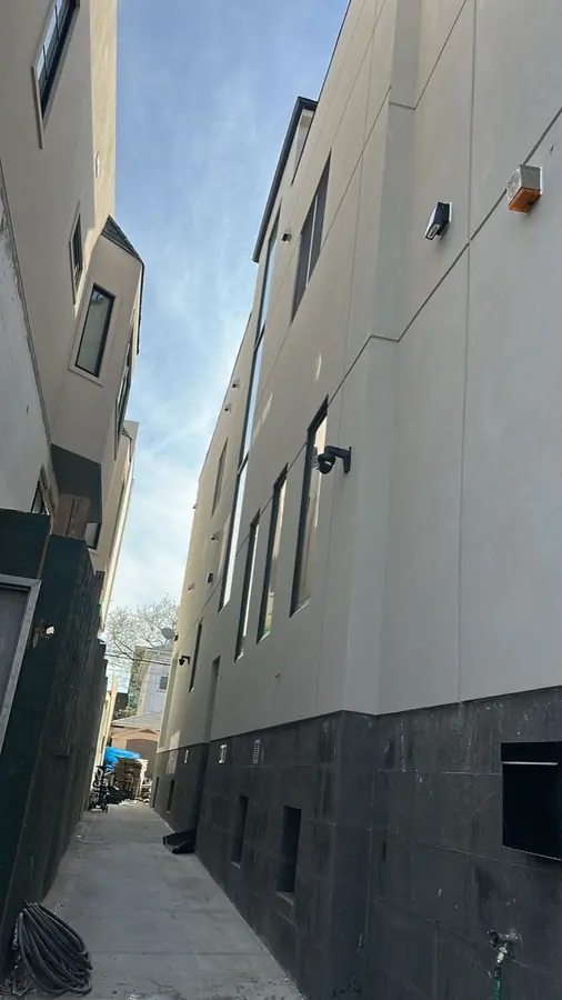 Stucco panel joints above a dark masonry base on a Brooklyn building