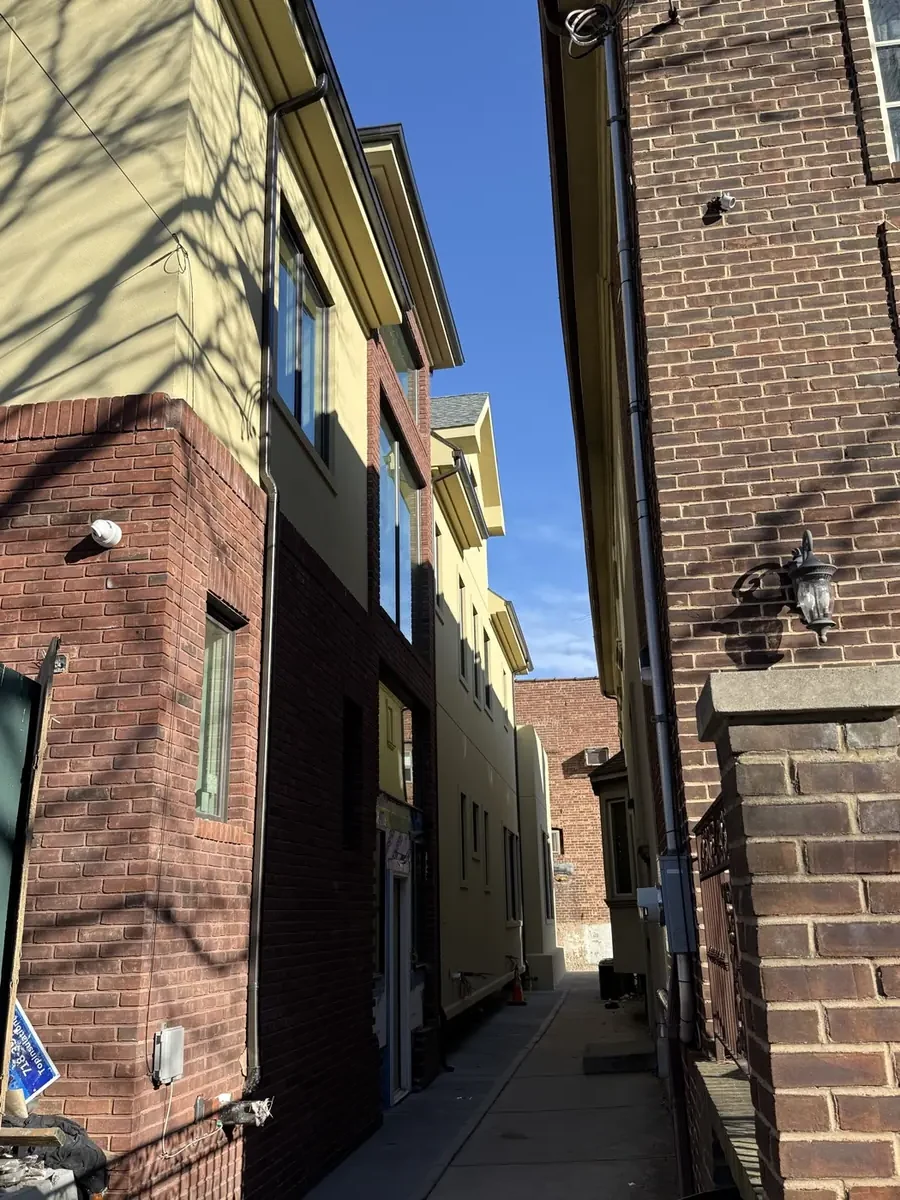 Downspout running the full height of a stucco wall in a narrow Brooklyn alley
