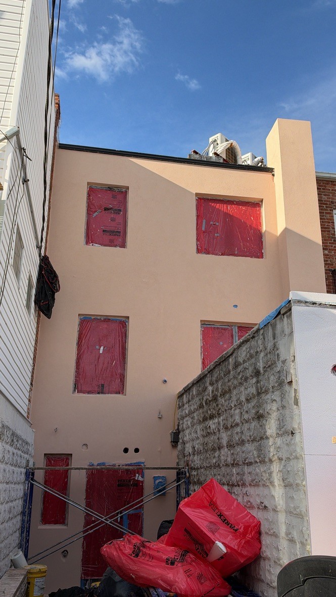 Stucco base coat applied to a Brooklyn wall with window openings masked and protected