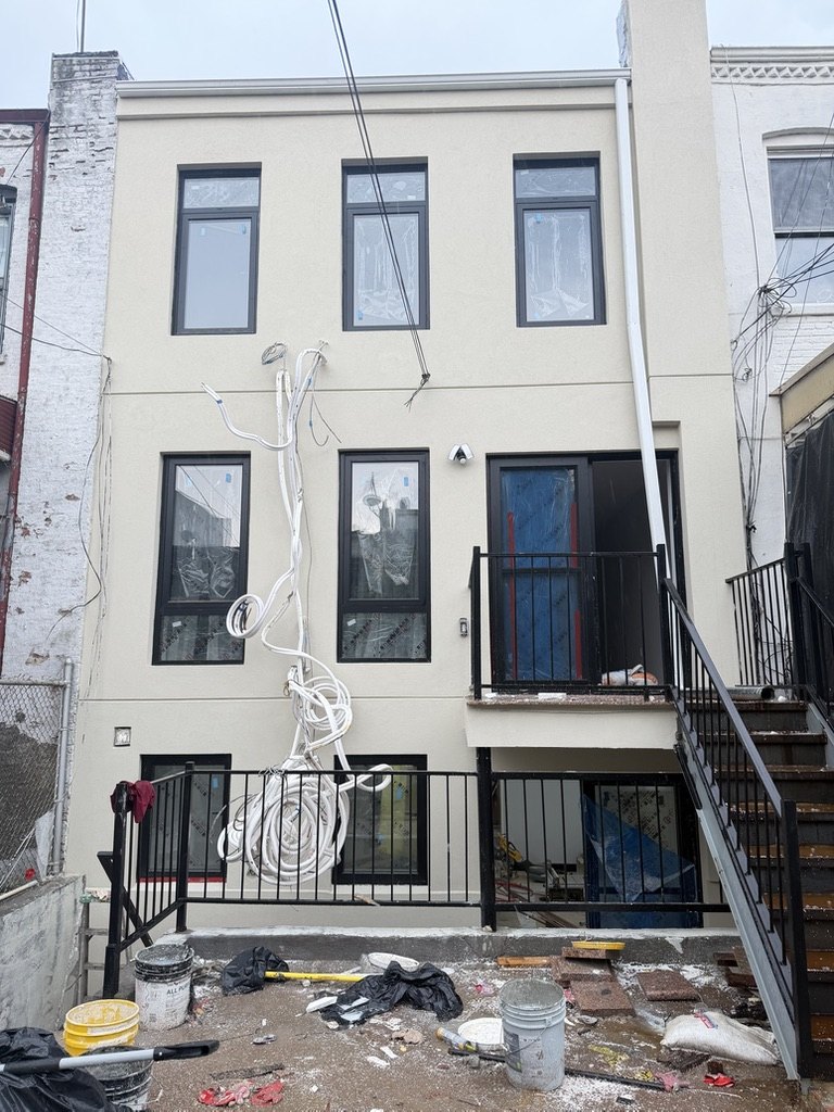 Completed three story stucco rear facade in Brooklyn with window openings and a parapet above