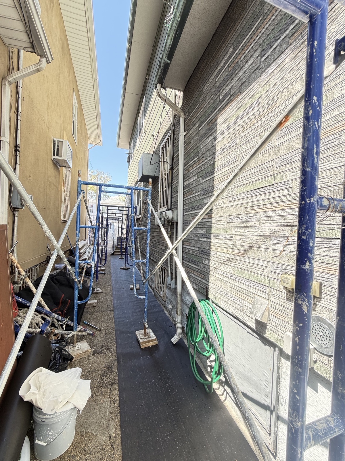 Scaffolding and ground protection set up on a narrow Brooklyn side alley for stucco work
