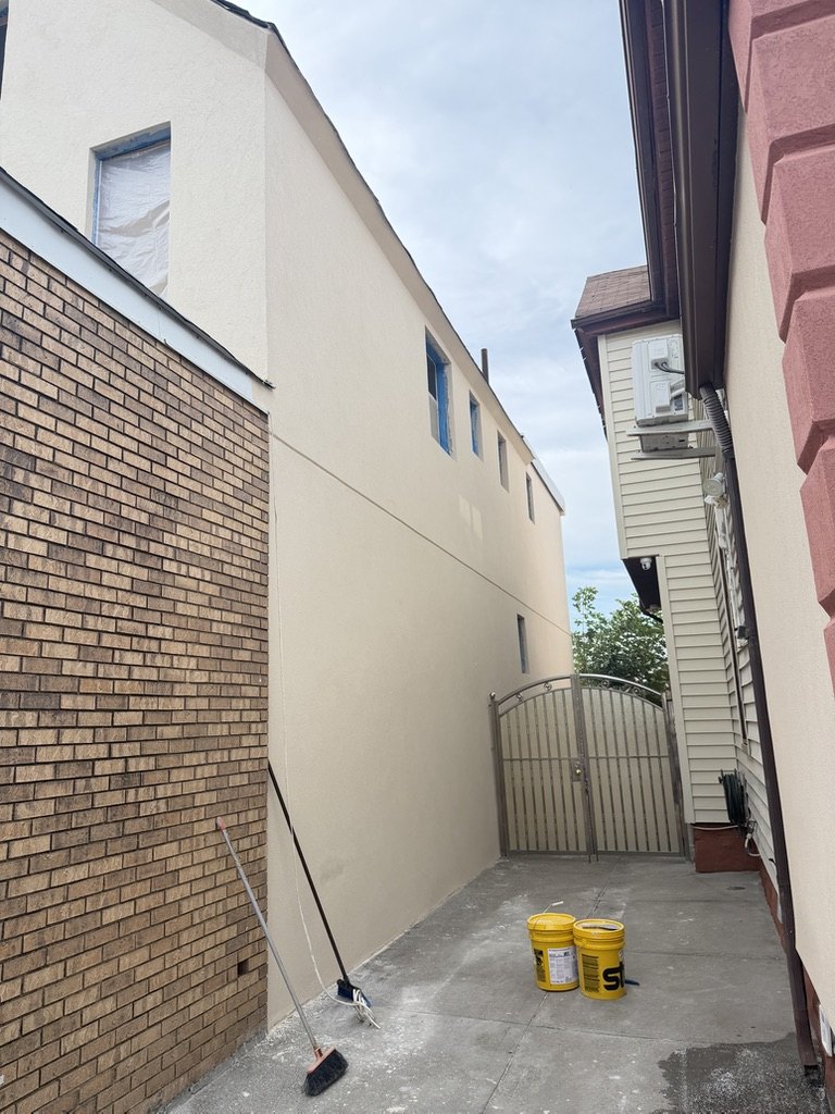 Finished stucco side wall running the length of a narrow Brooklyn alley between two buildings
